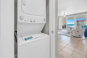 Ein Waschbereich mit Waschmaschine, Wäscheständer und Blick auf einen Balkon mit Pool und einem Gebäude im Hintergrund.