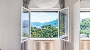 A room with a large window offering a view of a mountainous landscape and a lake. - General Terms and Conditions - Vacation Rental:Welcome to our vacation rental. To ensure a pleasant and hassle-free stay, please review the following general terms and conditions.Assistance ServicesIn-person assistance: Available from 9:00 AM to 6:00 PMT (Perledo)