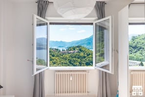 A room with a large window offering a view of a mountainous landscape and a lake. - General Terms and Conditions - Vacation Rental:Welcome to our vacation rental. To ensure a pleasant and hassle-free stay, please review the following general terms and conditions.Assistance ServicesIn-person assistance: Available from 9:00 AM to 6:00 PMT (Perledo)