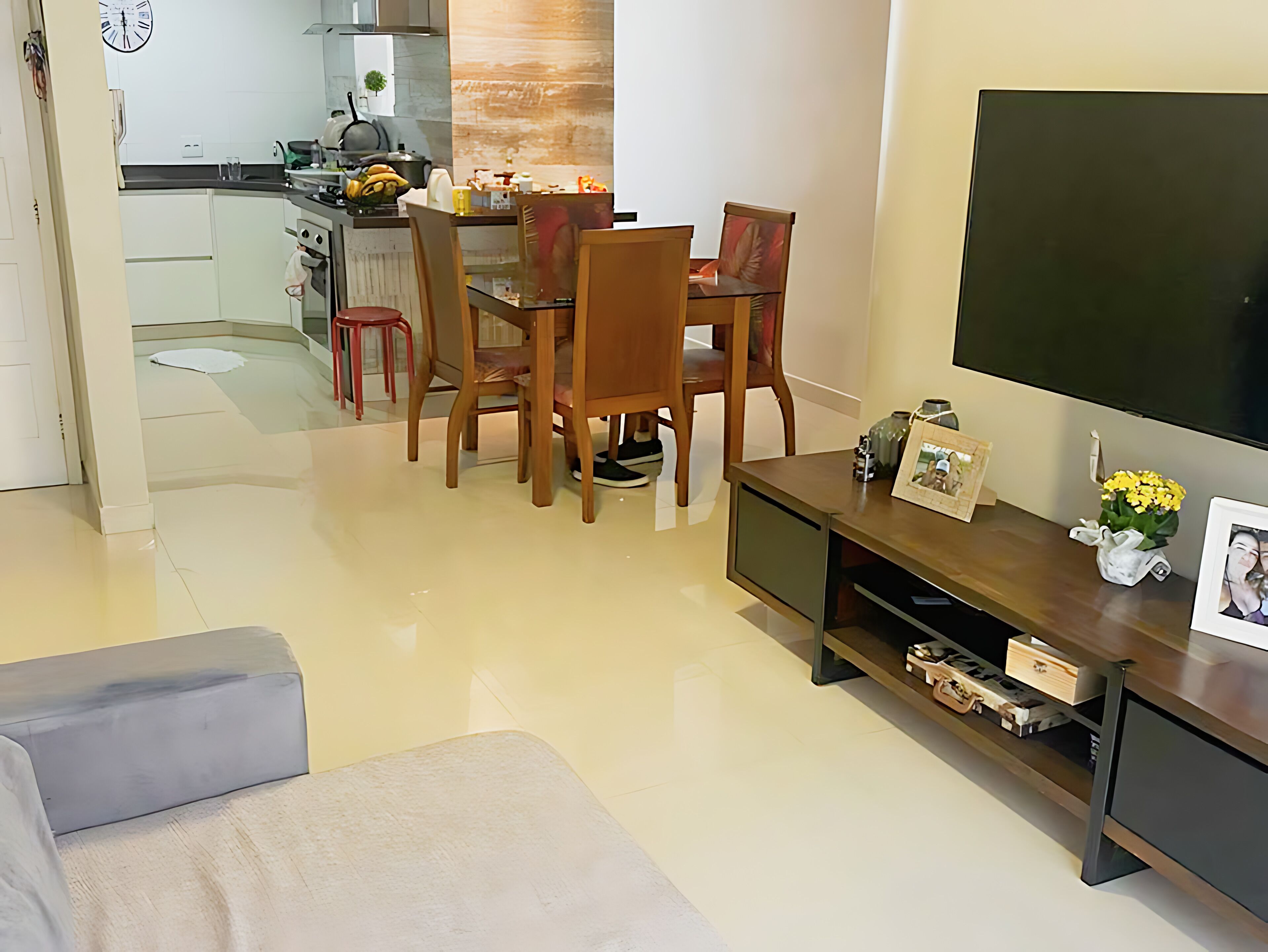 Een moderne woonkamer met een bank, een tv-meubel met een flatscreen televisie, een eethoek met een tafel en stoelen, en een keuken op de achtergrond.