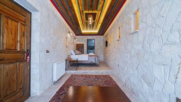 A room with a stone wall, wooden door, bed, and a large wooden table.