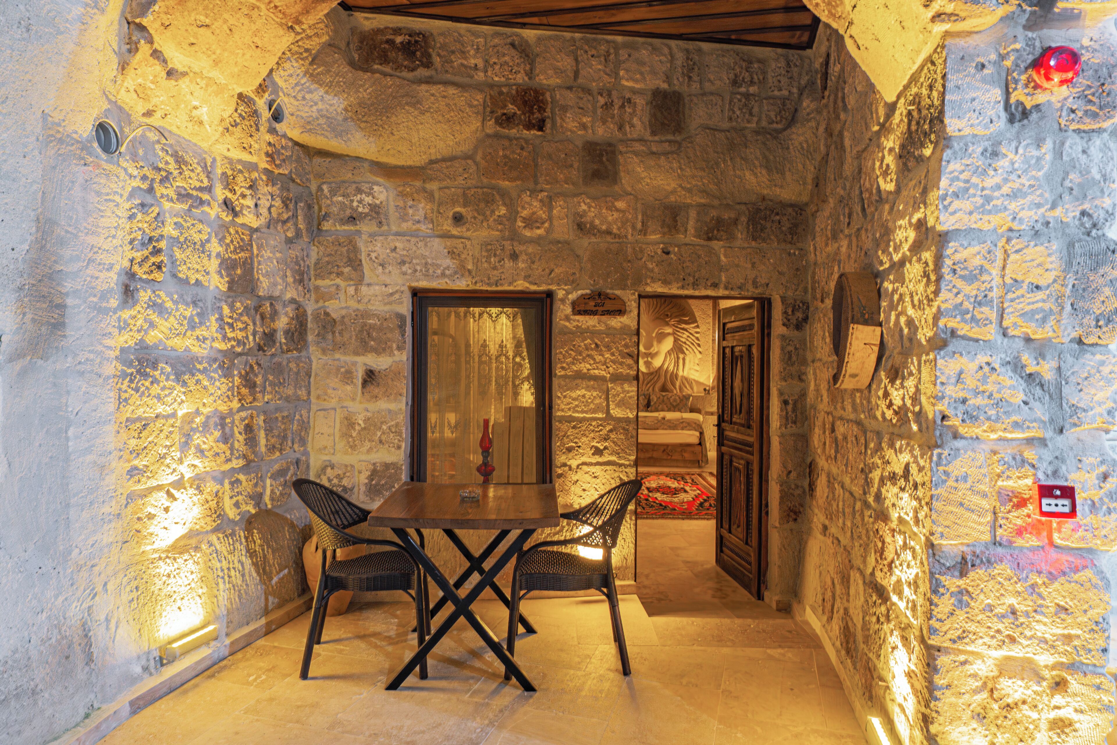 A stone-walled room with a table and chairs, a door leading to another room, and a red sign on the wall.