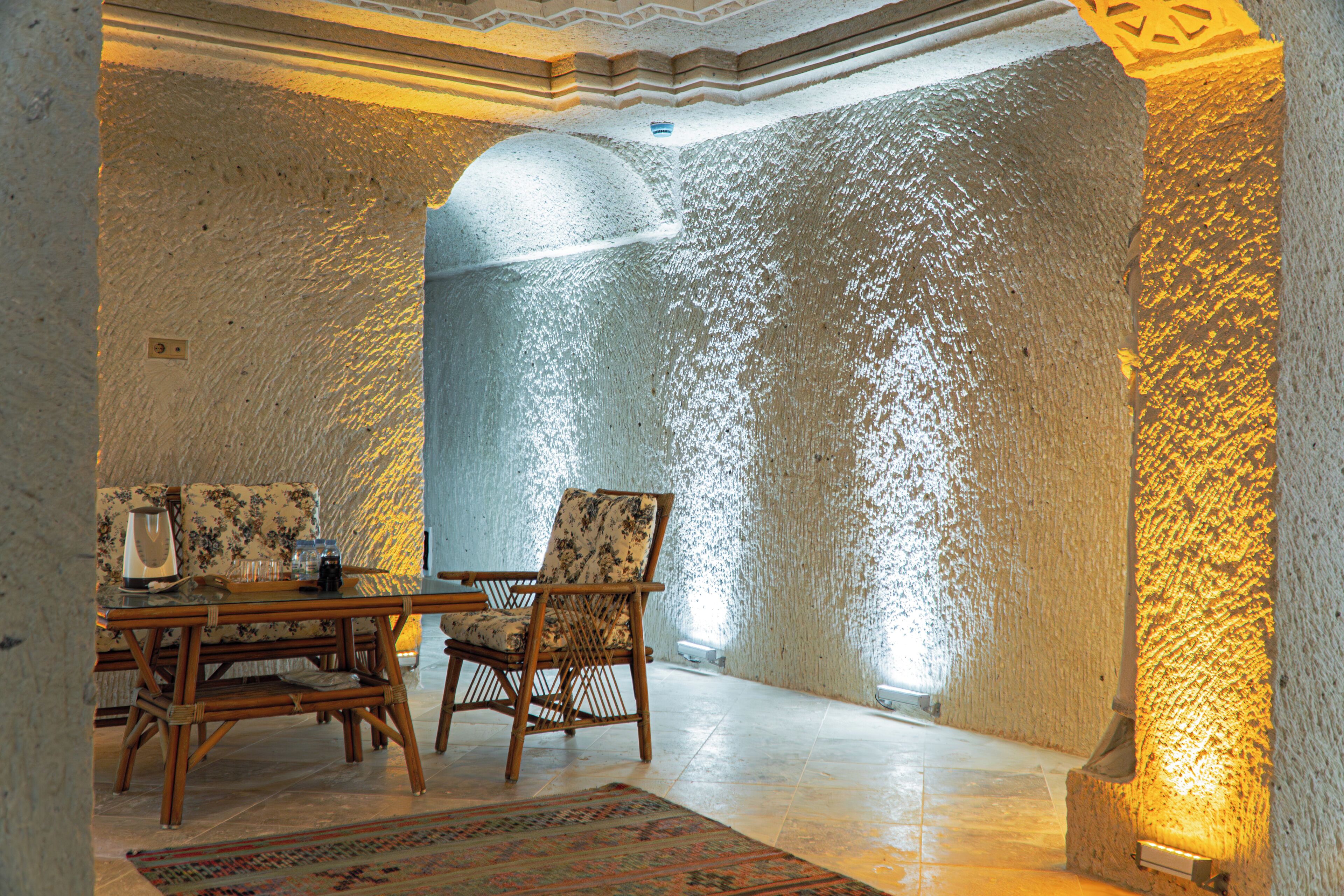 A room with a stone wall, a wooden table, two chairs, and a patterned rug.