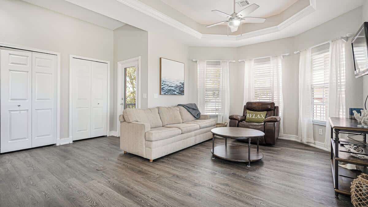 A living room with a sofa, armchair, round coffee table, and a ceiling fan.