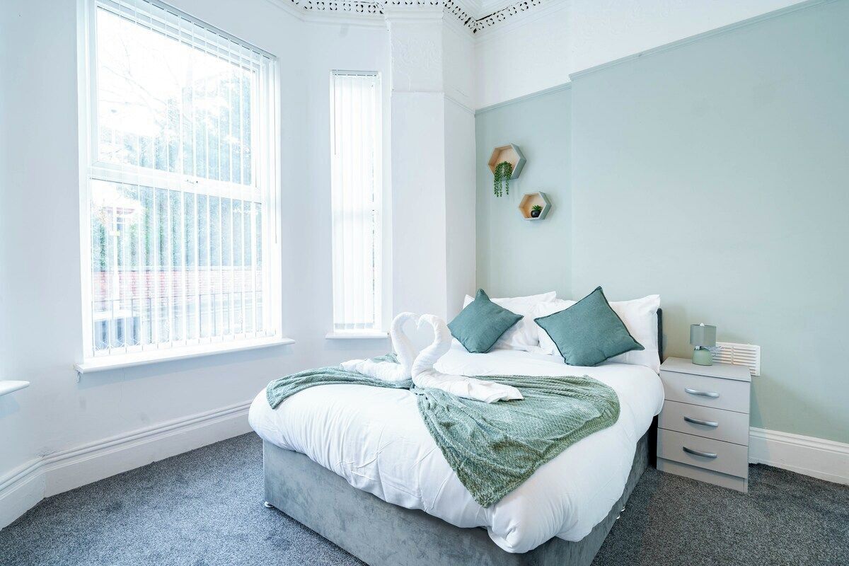 A bedroom with a bed, a nightstand, a window, and a wall-mounted shelf.
