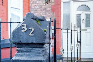 A black metal gate with the number 32, a white door with a window, and a brick wall in the background. - Birkenhead CH43 | Spacious 6BR Home | Sleeps 12 (Birkenhead)