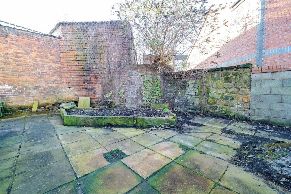 A courtyard with a brick wall, a stone wall, and a raised planter with plants.