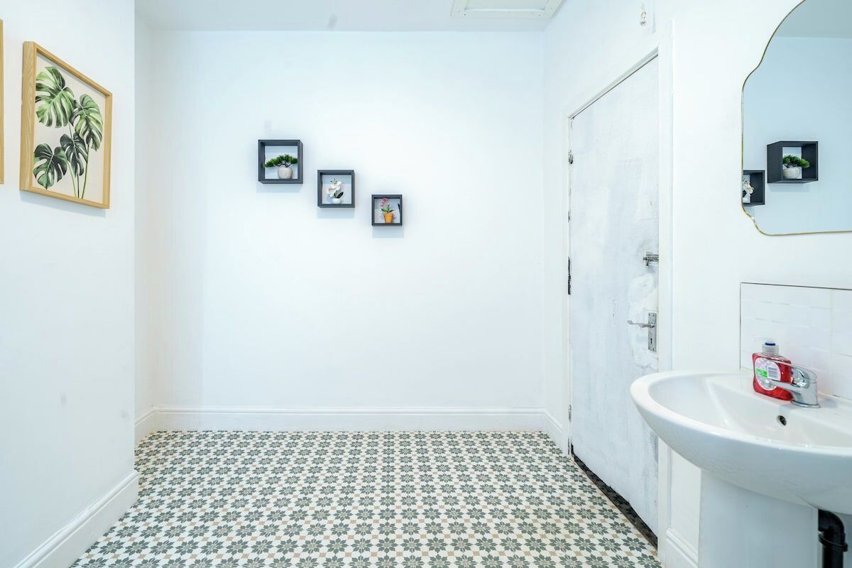 A bathroom with a white sink, a mirror, and a patterned floor. There are three framed pictures on the wall.