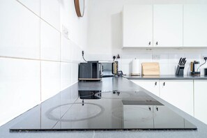 A modern kitchen with white cabinets, a black induction cooktop, a toaster, and a knife block. - Birkenhead CH43 | Spacious 6BR Home | Sleeps 12 (Birkenhead)