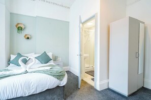 Una camera da letto con un letto, un armadio, un bagno con doccia e uno scaffale a muro con piante.