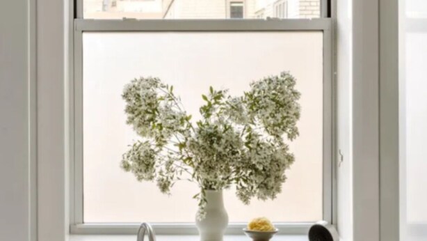 Ein modernes Badezimmer mit einem großen Fenster, einem weißen Waschbecken und einer Topfpflanze.