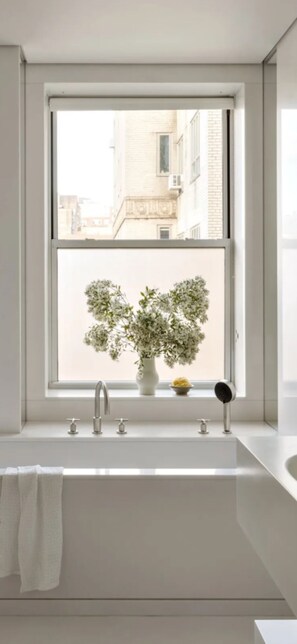 Een moderne badkamer met een groot raam, een witte wastafel en een potplant.