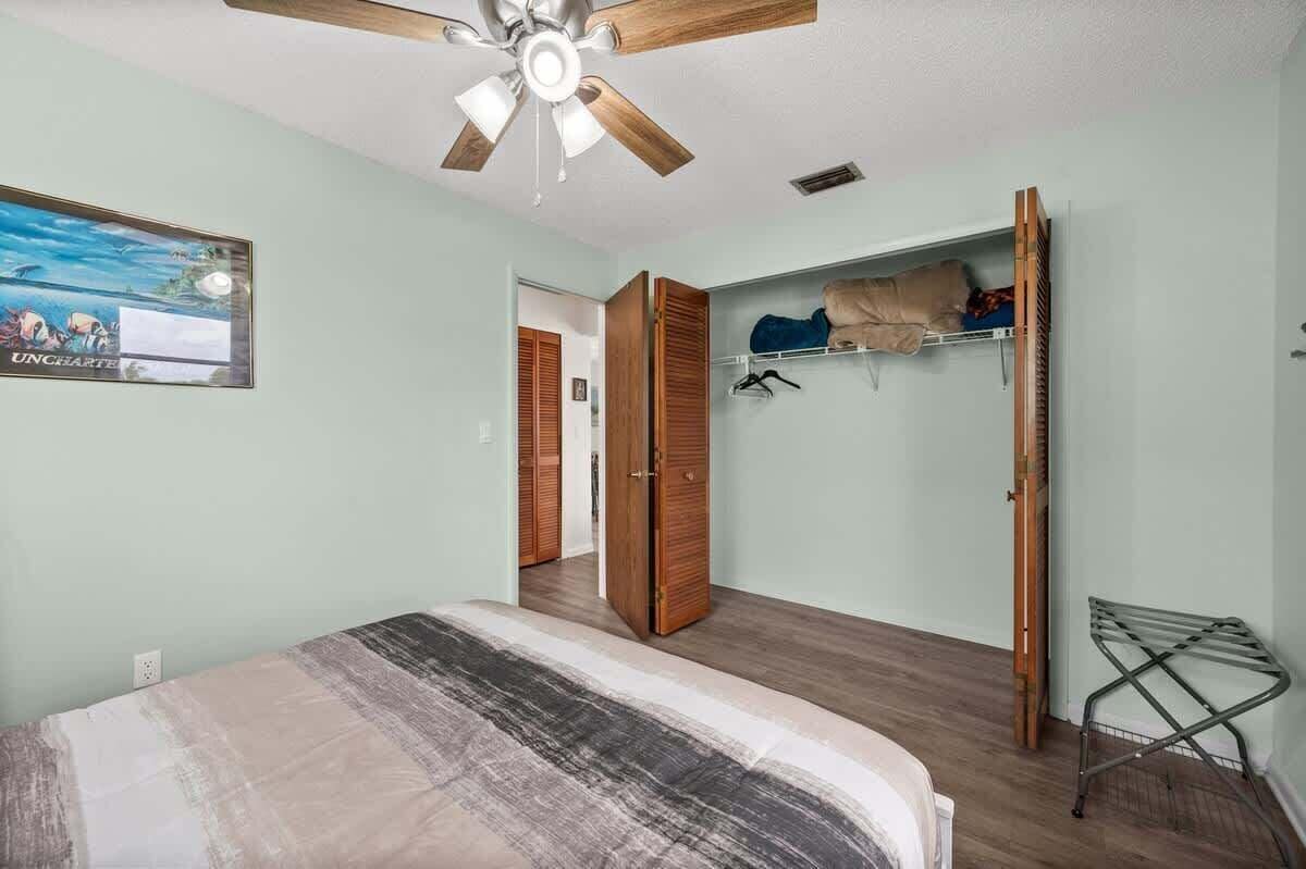 A bedroom with a bed, a ceiling fan, a wardrobe, a drying rack, and a painting on the wall.