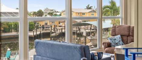 Una habitación con amplios ventanales que dan a un puerto deportivo, un sofá azul a rayas y un sillón marrón.
