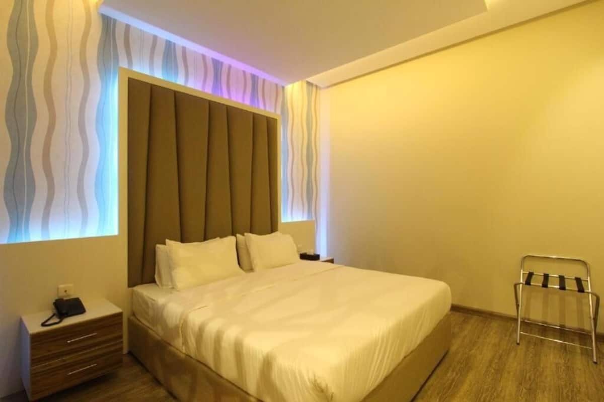 A hotel room with a large bed, a nightstand, a chair, and a wall with a wavy pattern.