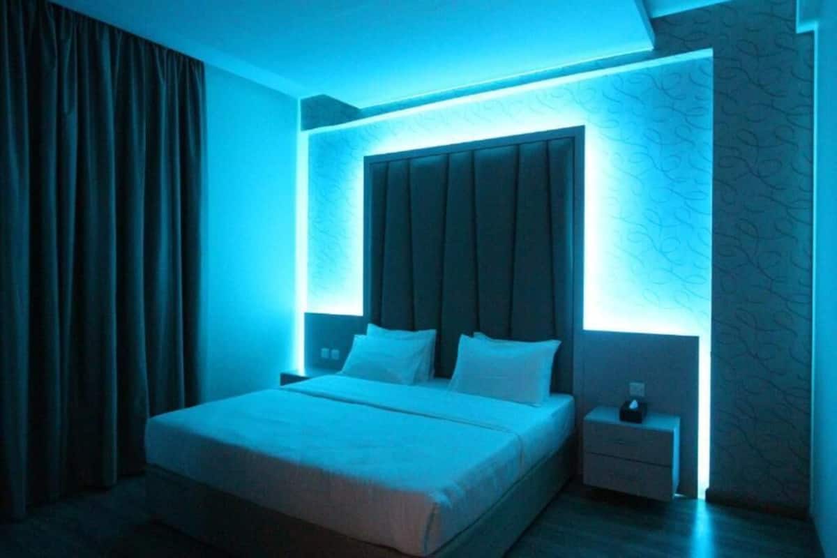 A modern bedroom with a large bed, a nightstand, and a wall-mounted headboard.
