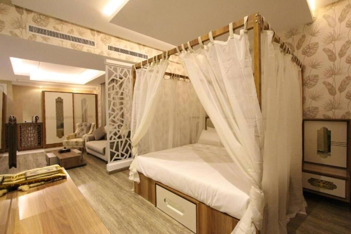 A four-poster canopy bed with a wooden frame and white bedding, a small bedside table, and a nightstand with a lamp.