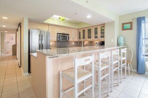 A modern kitchen with a central island, stainless steel appliances, and a breakfast bar with chairs. - Bubbles Up ~ Beachfront & Top Corner Balcony (Folly Beach)