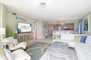 A spacious living room with a large TV, a dining area, and a kitchen. - Bubbles Up ~ Beachfront & Top Corner Balcony (Folly Beach)