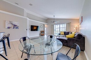 Ein modernes Wohnzimmer mit einem Glastisch, einer Couch und einem an der Wand befestigten Fernseher.