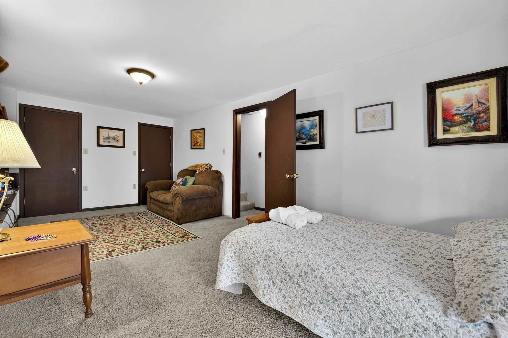 A hotel room with a bed, a desk, a chair, and a door leading to another room.
