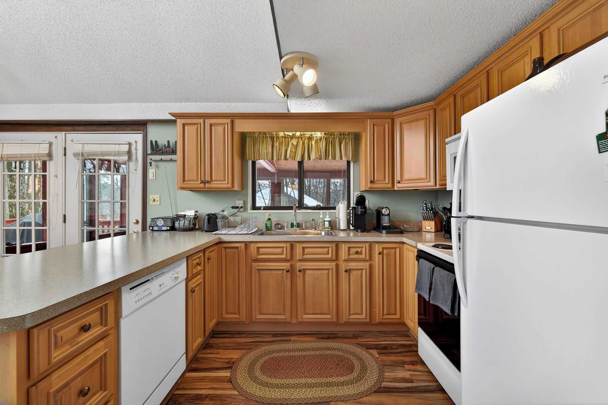 A kitchen with wooden cabinets, a white refrigerator, a dishwasher, and a window with a curtain.