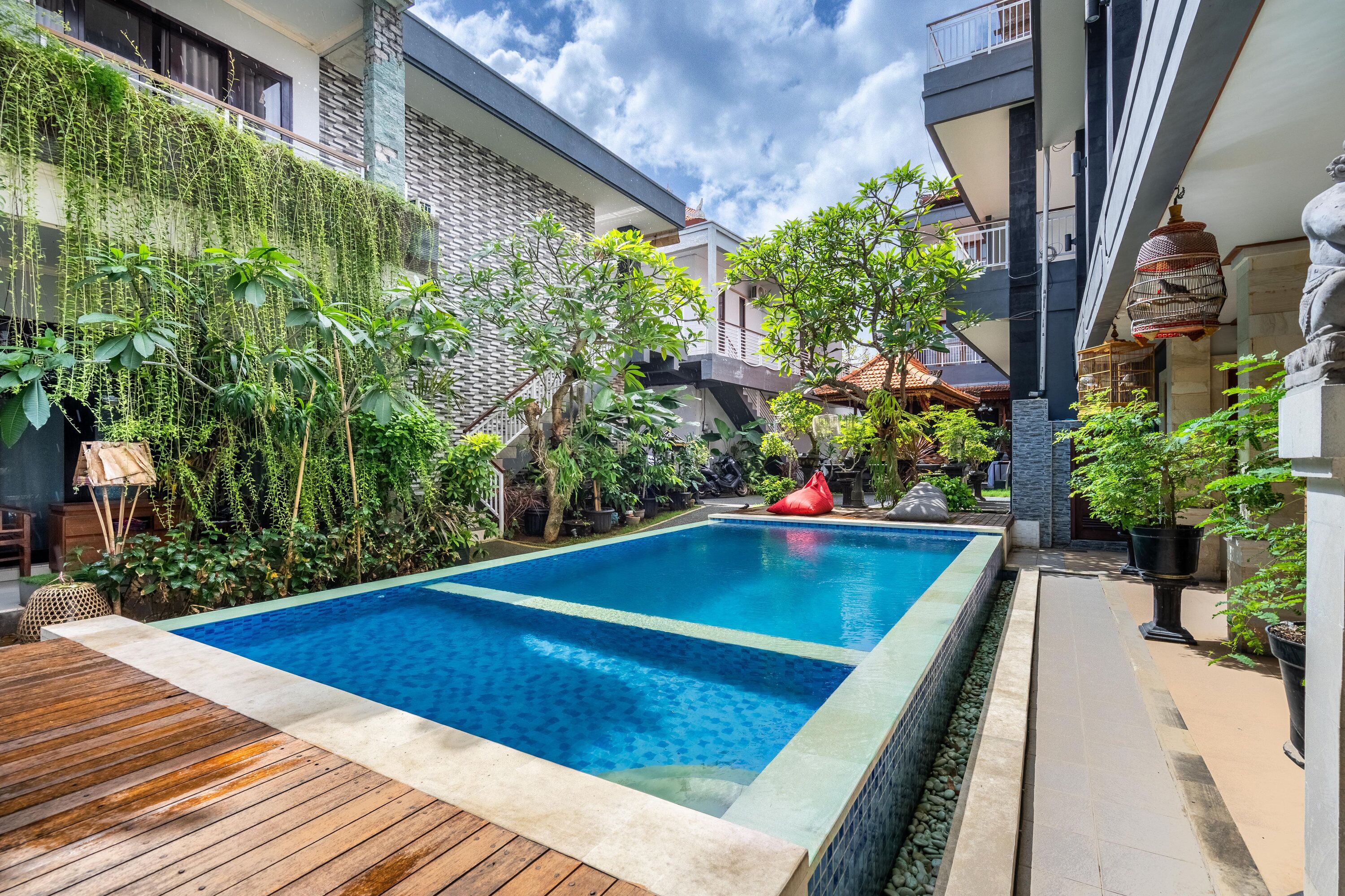 A swimming pool with a wooden deck, surrounded by lush greenery and potted plants.