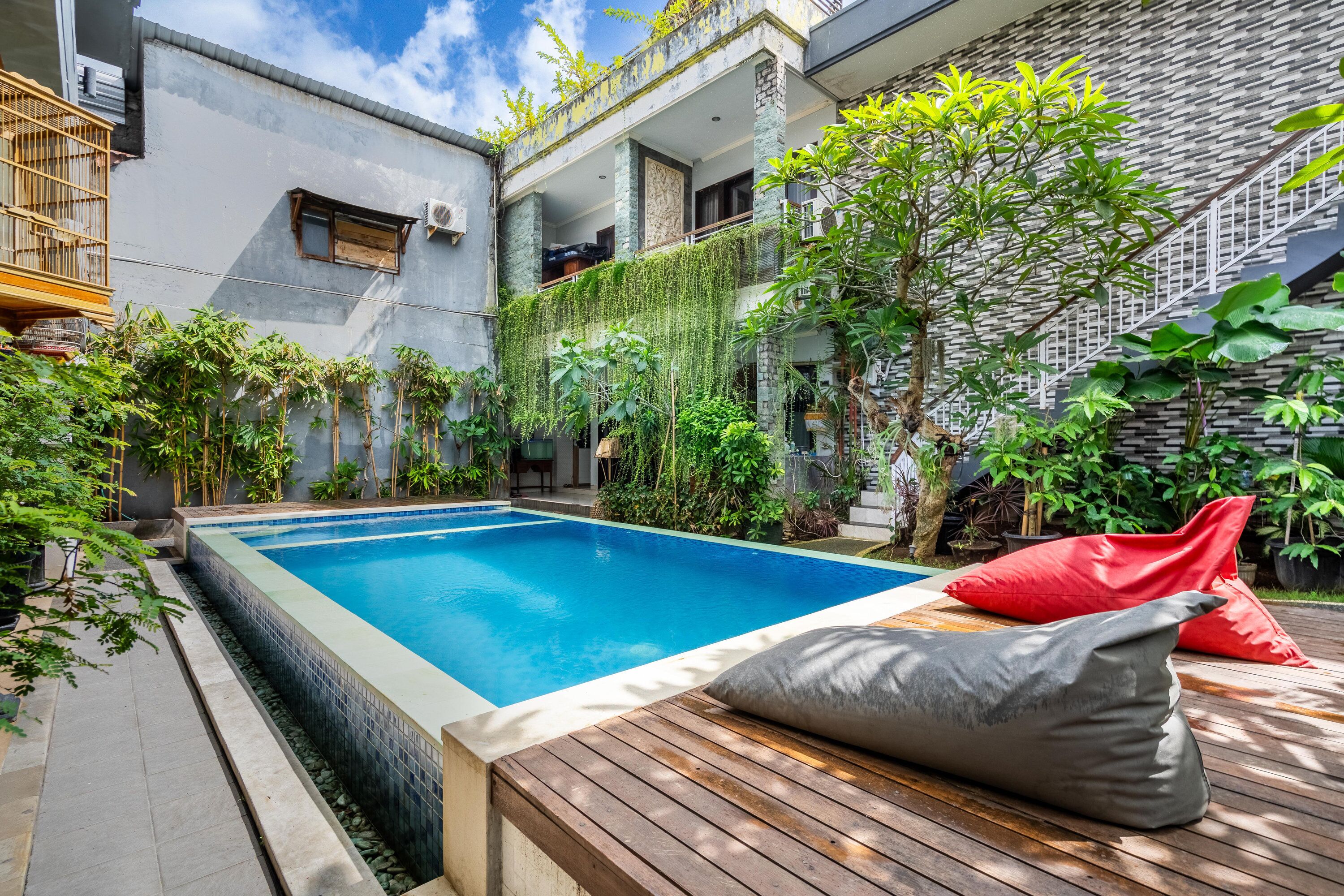 A swimming pool with a wooden deck and a red and gray cushion.