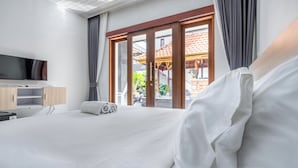 Habitación de hotel con cama, televisor montado en la pared, aparador de madera y vista a un espacio exterior con un edificio tradicional.