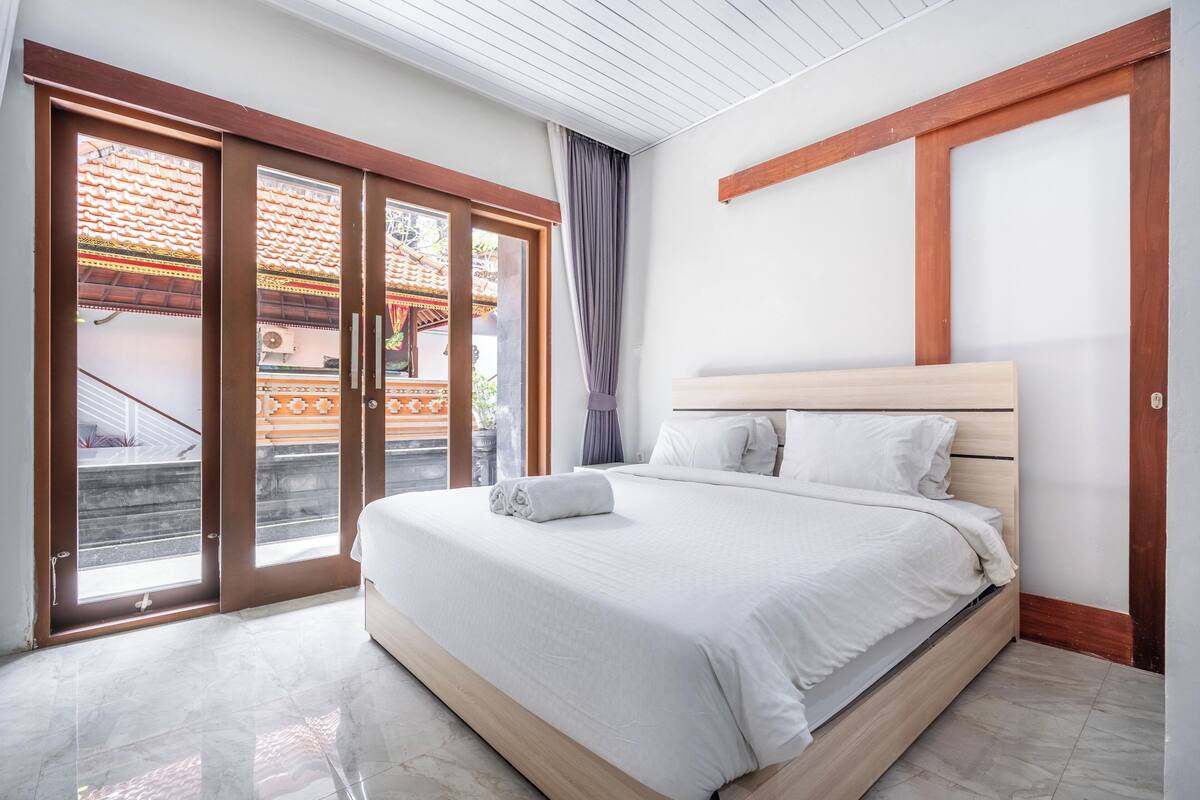 A bedroom with a large bed, a wooden headboard, and a sliding glass door leading to an outdoor area.