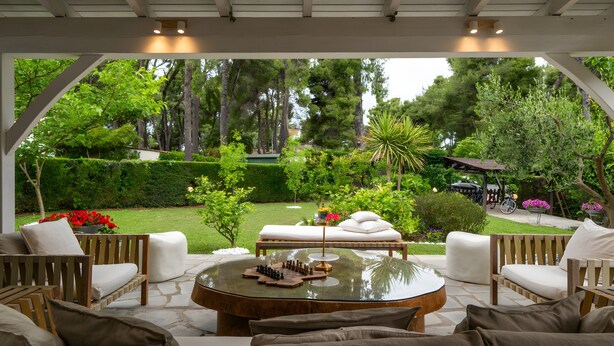 An outdoor seating area with a round table, cushioned chairs, and a chessboard.
