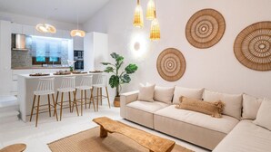 A modern living room with a sofa, a wooden coffee table, and a kitchen area with bar stools.