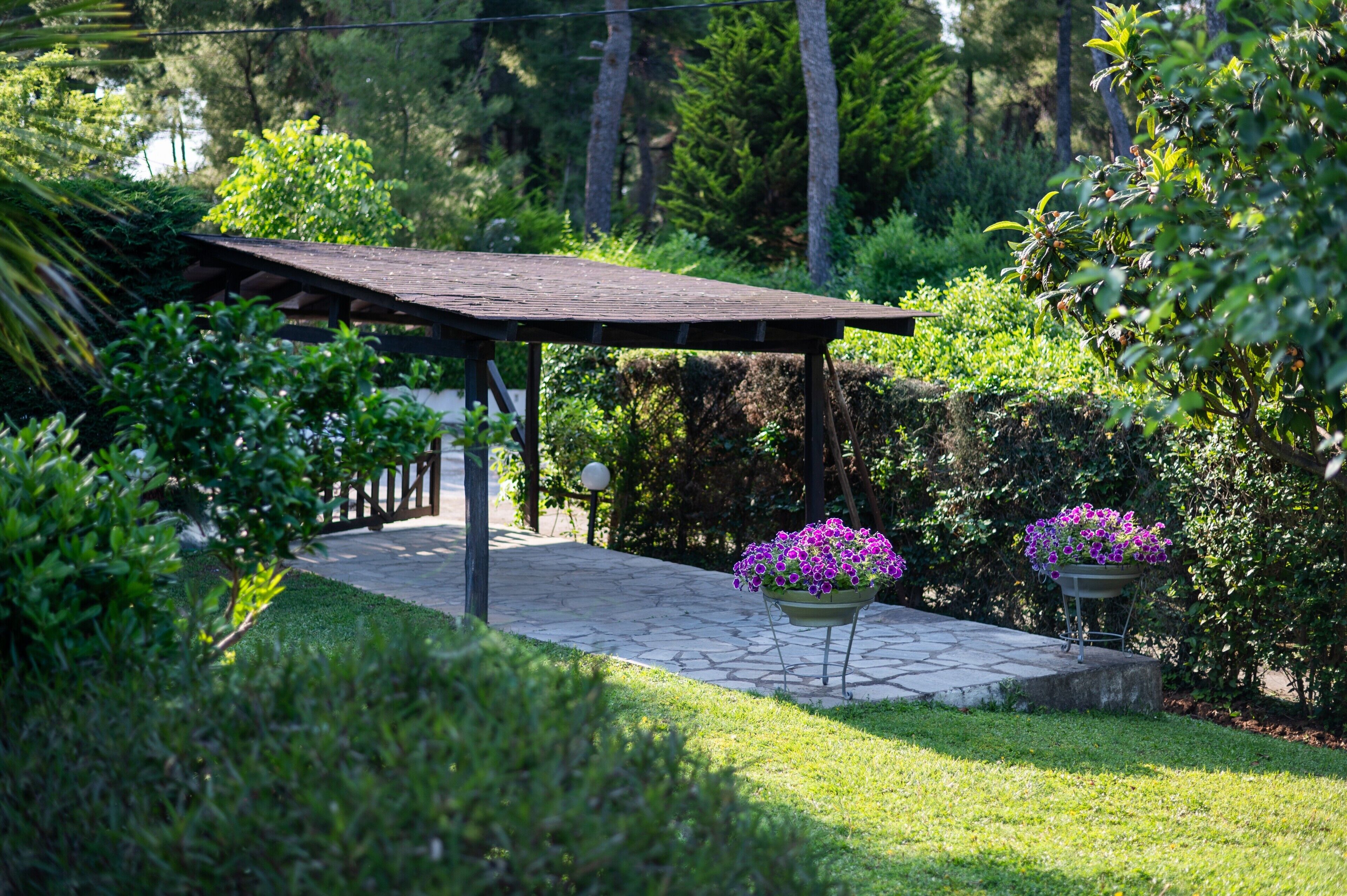 A garden with a wooden pergola, stone pathway, and potted purple flowers.
