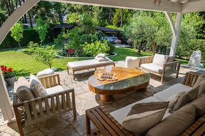 Um pátio externo com mesa de xadrez, assentos acolchoados e vista para o jardim.