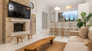 A modern living room with a stone fireplace, a flat-screen TV, a wooden bench, and a sofa.