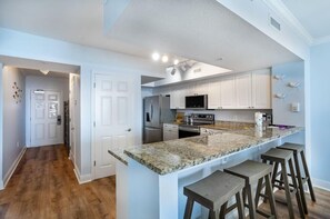 Eine moderne Küche mit weißen Schränken, Granit Arbeitsplatten und Edelstahlgeräten. Es gibt drei Barhocker und eine große Kücheninsel.