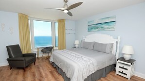 A bedroom with a bed, a chair, a nightstand, a lamp, and a view of the ocean. - ☀️Gulf FRONT-Pools+Hot Tubs-Emerald Beach 2030☀️ (Panama City Beach)