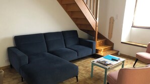A living room with a sectional sofa, a coffee table, a pink chair, and a wooden staircase. - Gîte Le Colombet Au Coeur du Périgord Noir (Audrix)