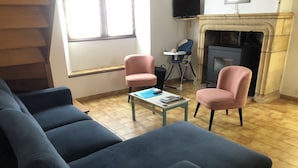 A living room with a blue sofa, two pink chairs, a small table with a remote control, and a fireplace. - Gîte Le Colombet Au Coeur du Périgord Noir (Audrix)