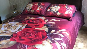 A bed with a floral bedspread, a wooden headboard, and a nightstand with a lamp. - Gîte Le Colombet Au Coeur du Périgord Noir (Audrix)