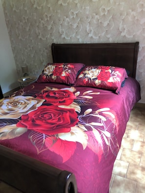 Un lit avec une couvre-lit Ă motifs floraux, une tĂȘte de lit en bois et une table de chevet avec une lampe.