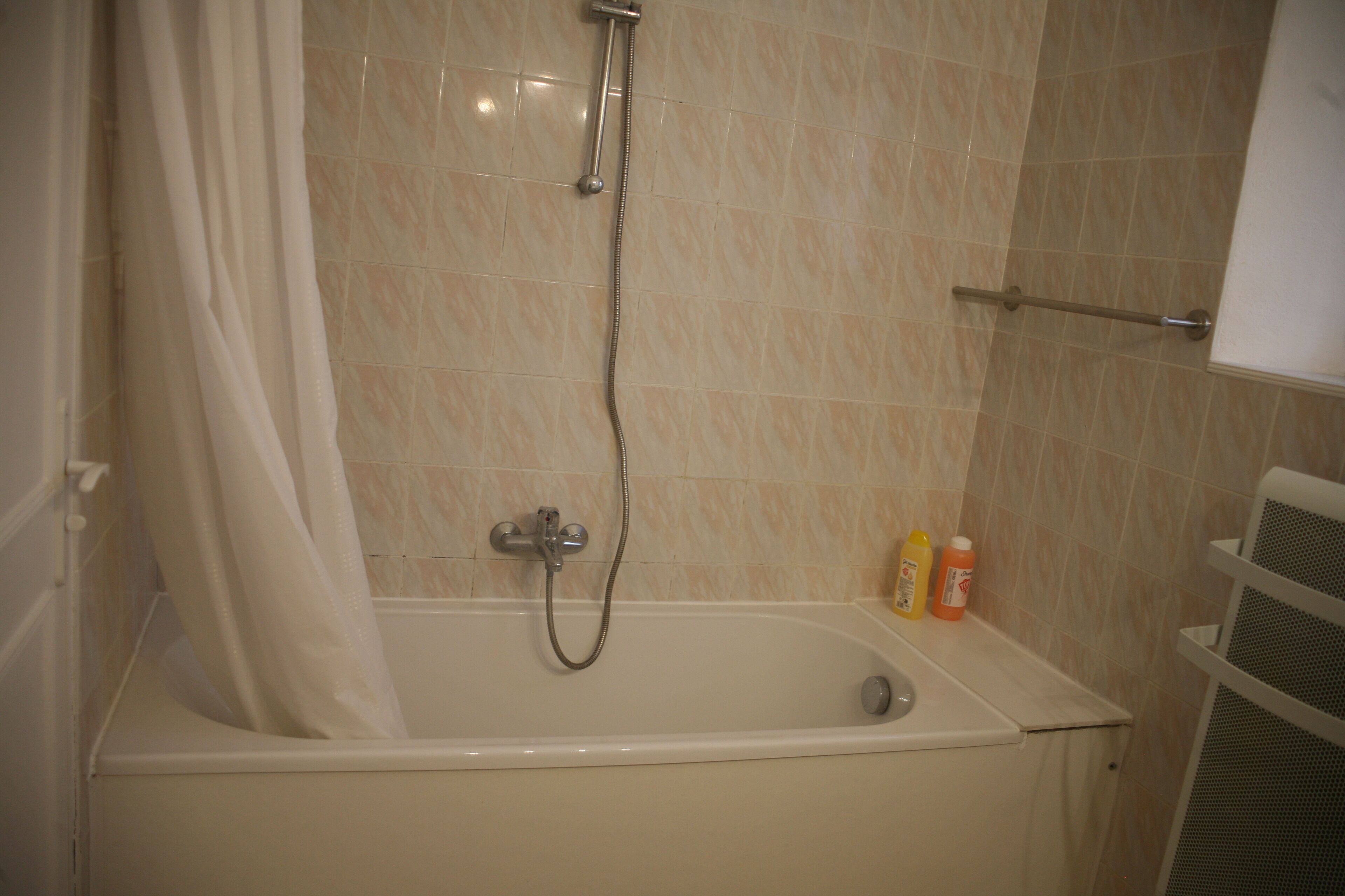Un baño con bañera, ducha y dos botellas de champú a un lado.