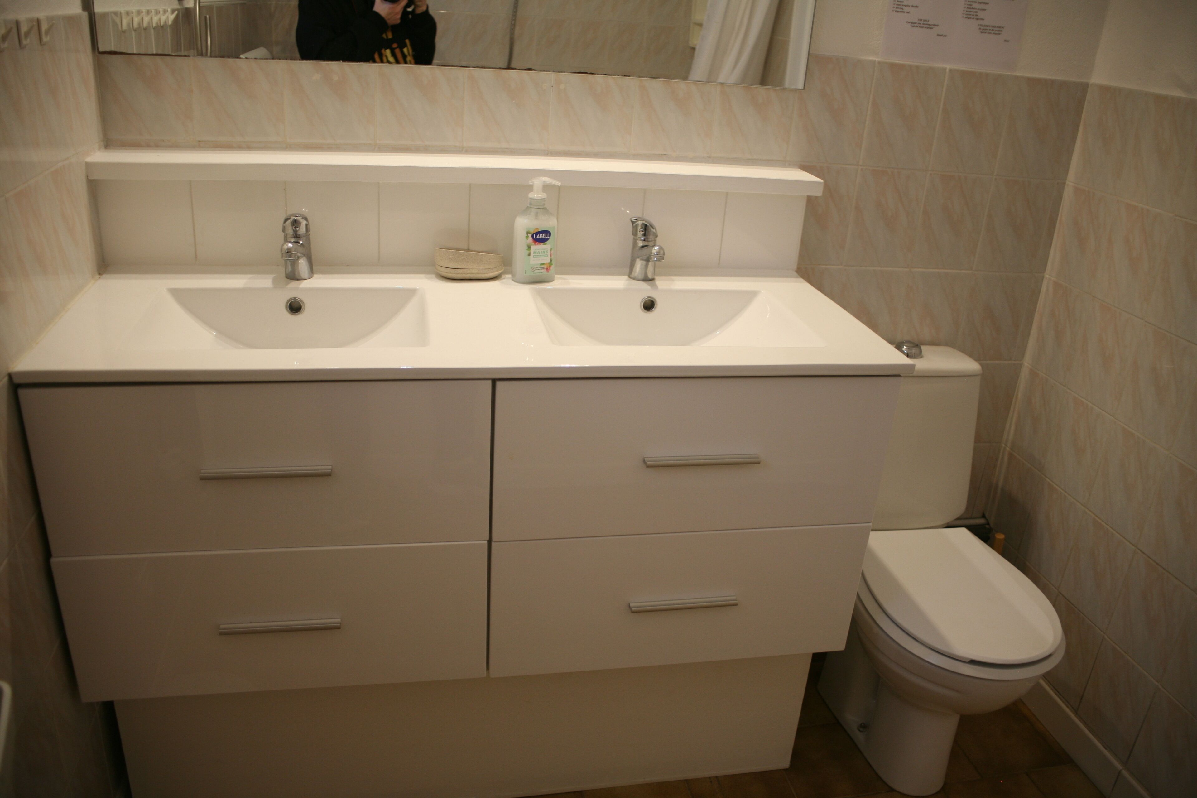 Een badkamer met twee wasbakken, een toilet en een spiegel boven de wasbakken.
