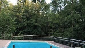A rectangular swimming pool surrounded by a wire fence, with a grassy area in the foreground and dense trees in the background. - Gîte Le Colombet Au Coeur du Périgord Noir (Audrix)