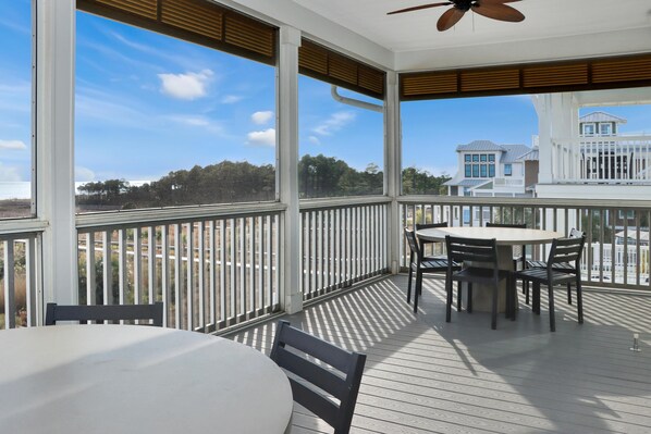 A covered outdoor area with a table and chairs, large windows, and a view of buildings and trees. - Southern Charm (Port St. Joe)