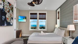 A modern hotel room with a large bed, a flat-screen TV, a desk with a lamp, and a view of the ocean through the windows. - Southern Charm (Port St. Joe)