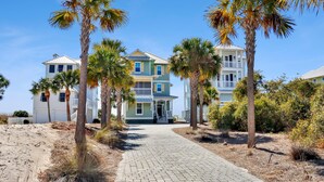 A beachfront property with a paved walkway leading to a two-story building, surrounded by palm trees and sandy terrain. - Southern Charm (Port St. Joe)