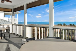 Un espacio al aire libre techado con una mesa y sillas, con vista a la playa.