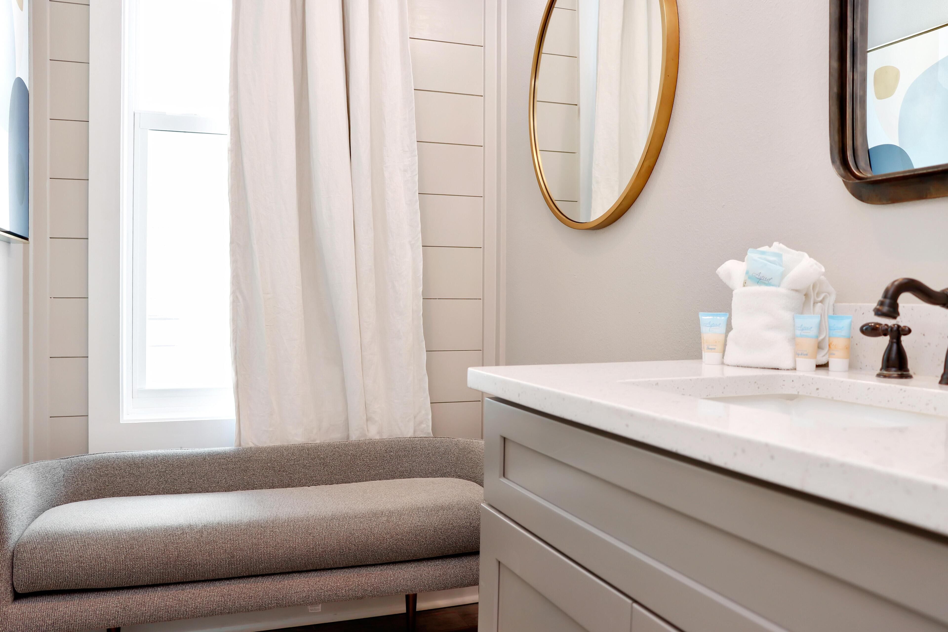 A bathroom with a white vanity, a mirror, and toiletries on the counter.