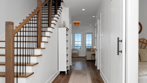 A modern interior with a wooden staircase, white walls, and a view to the outside. - West Wind (Port St. Joe)